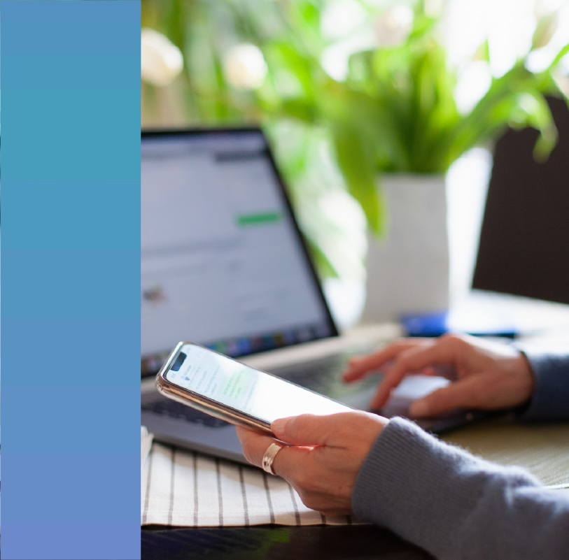 Person using a mobile phone while typing on a laptop.