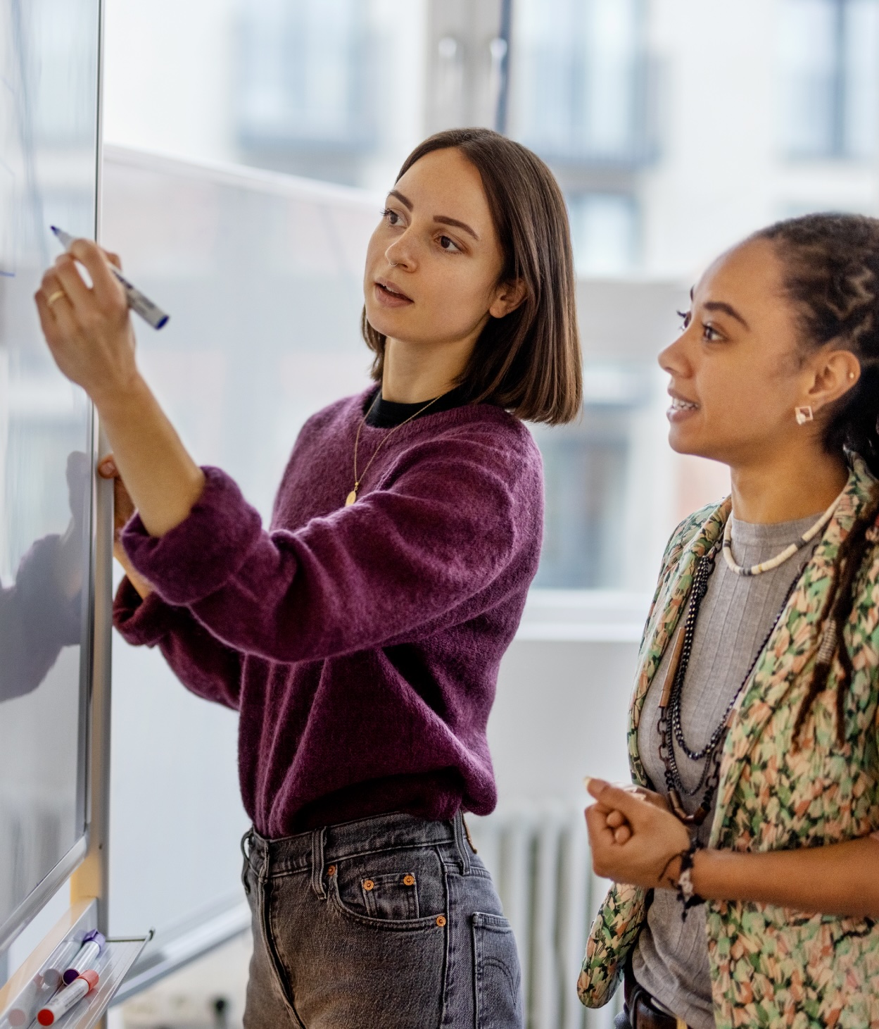 Woman writes on a whiteboard during a planning session with her coworker.